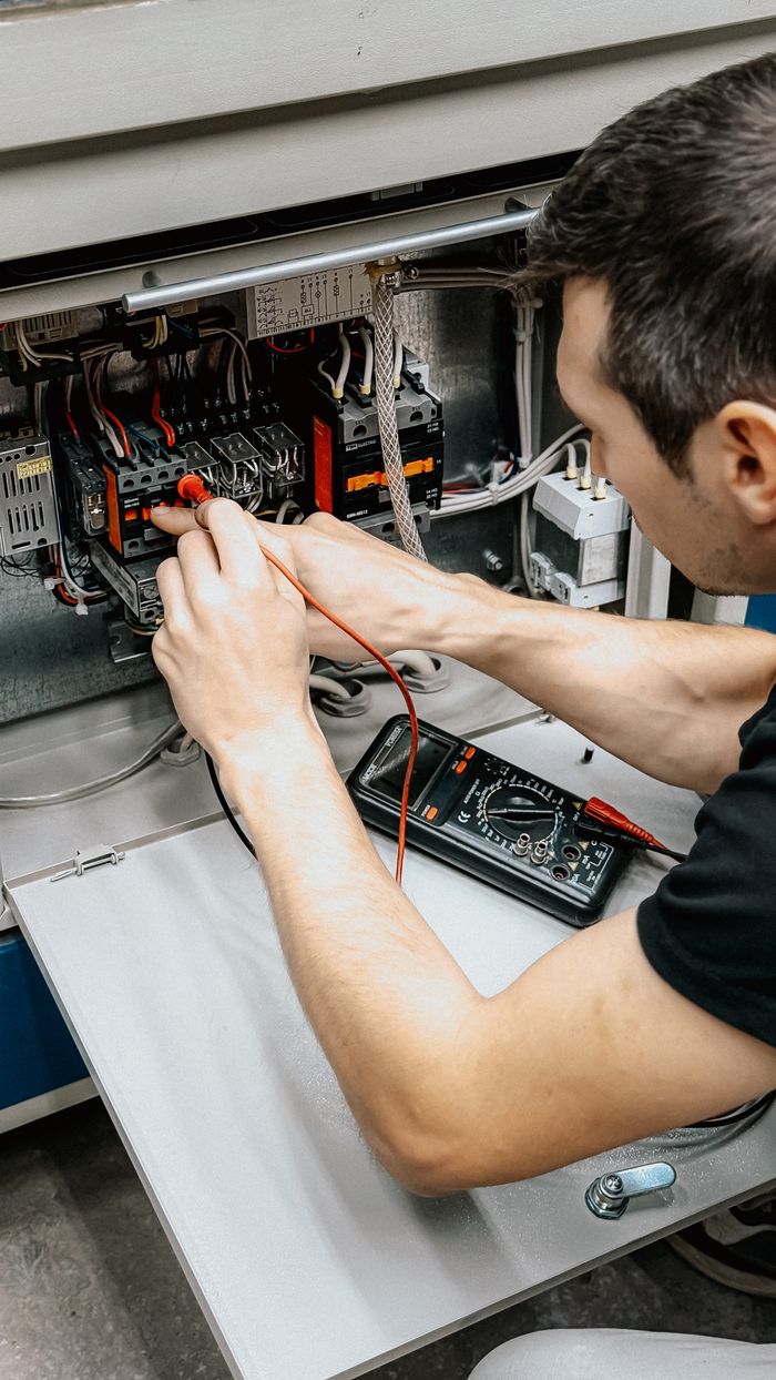 Services An electrician uses a multimeter to test and diagnose connections in an open electrical panel.